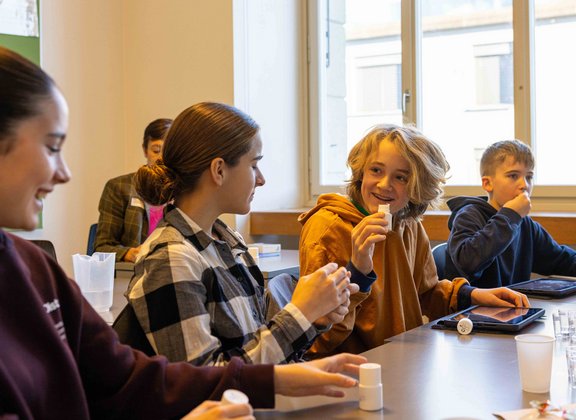 Schüler:innen in einem Klassenzimmer experimentieren am TecDay und lachen.