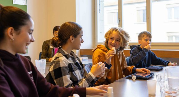 Schüler:innen in einem Klassenzimmer experimentieren am TecDay und lachen.