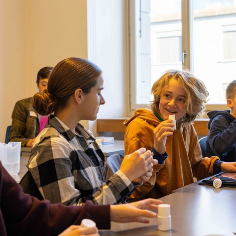 Schüler:innen in einem Klassenzimmer experimentieren am TecDay und lachen.