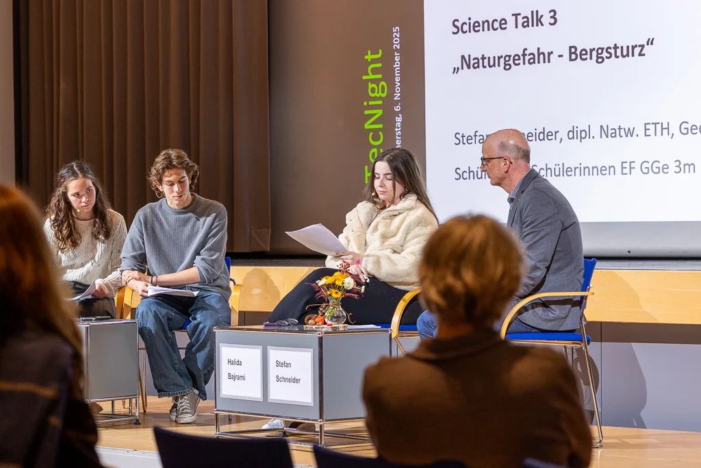 Discussione sul tema dei rischi naturali con tre studenti a sinistra e un esperto a destra del palco.